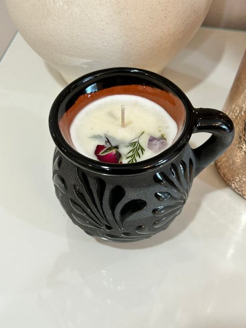 Decorative talavera candle in a black, ceramic, Mexican container with intricate patterns on a neutral background.