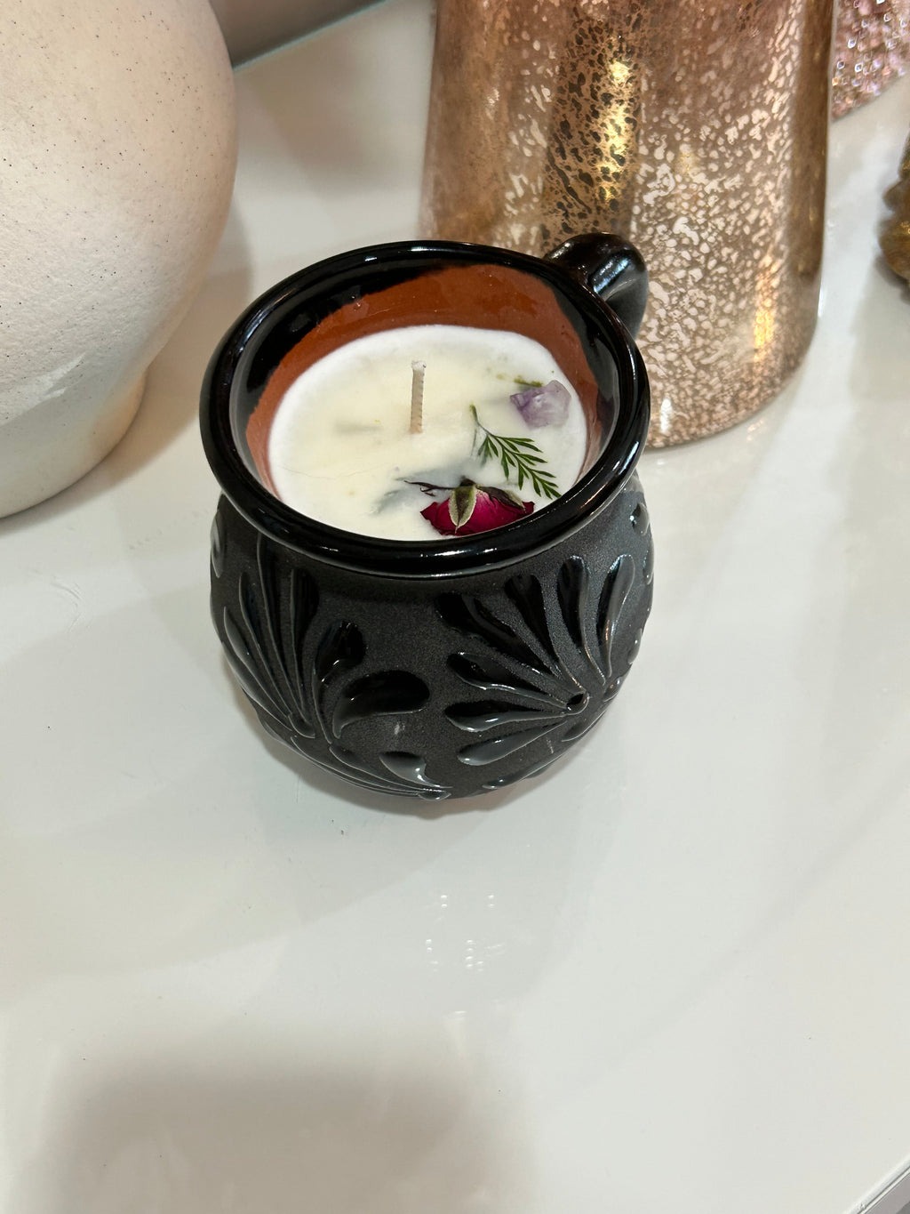 Decorative talavera candle in a black, ceramic, Mexican container with intricate patterns on a neutral background.