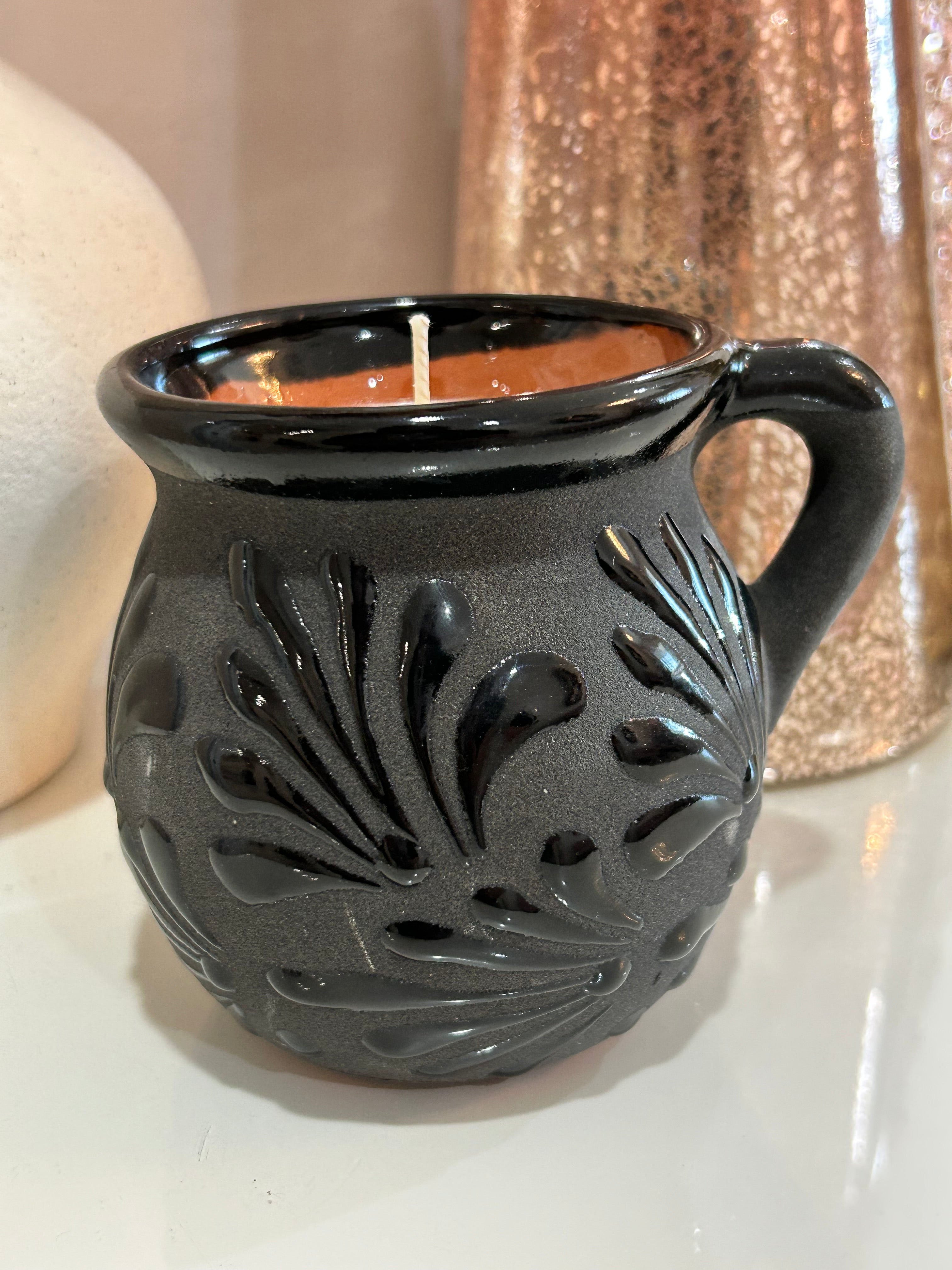 Decorative talavera candle in a black, ceramic, Mexican container with intricate patterns on a neutral background.