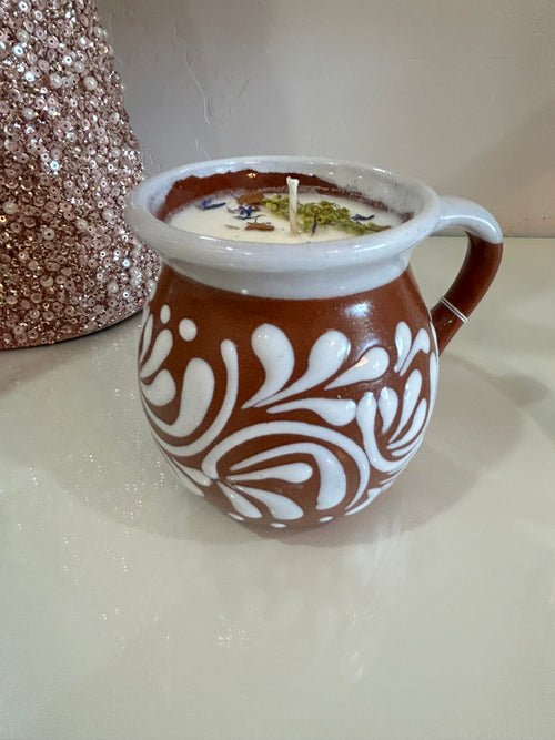 Decorative talavera candle in a terra-cotta brown, ceramic, Mexican container with intricate patterns on a neutral background.