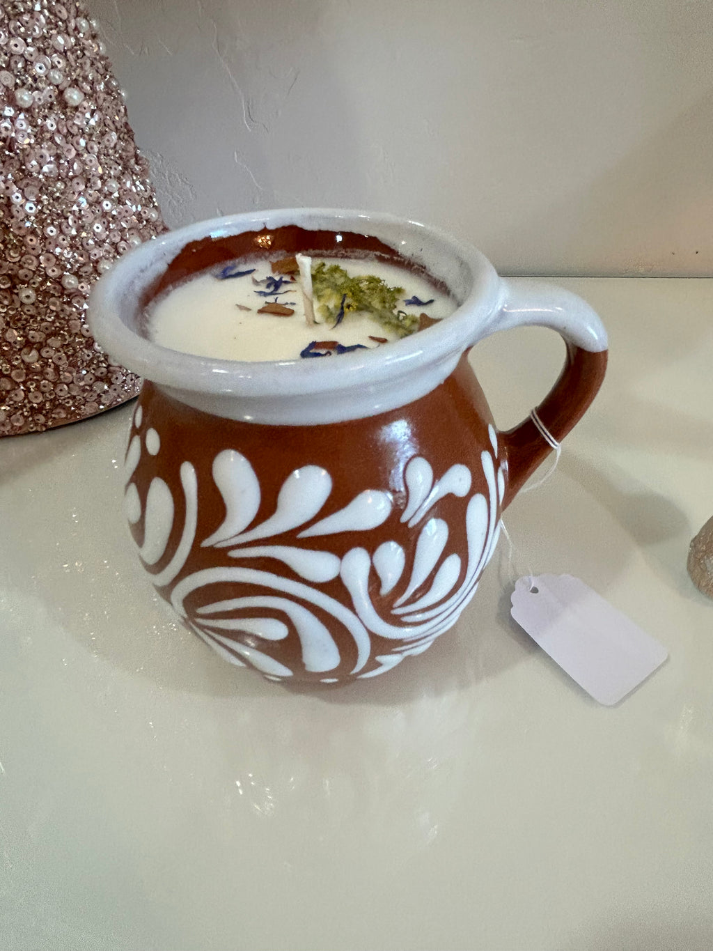 Decorative candle in a ceramic Mexican container with intricate patterns on a neutral background.
