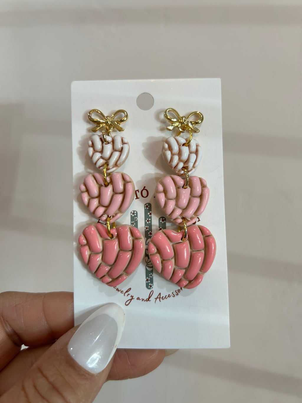 Set of pink and gold concha heart earrings on a backing card held by a hand.