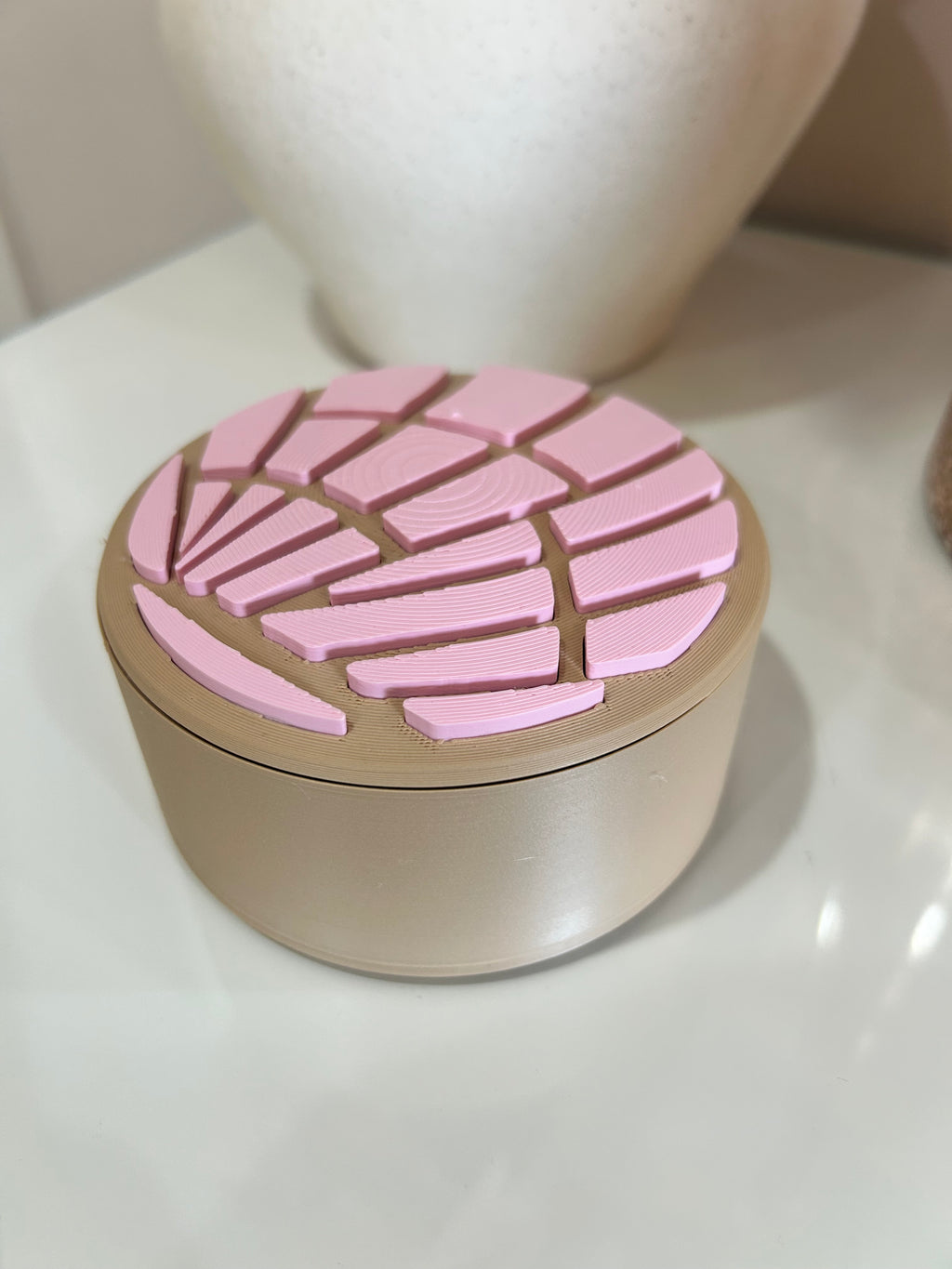 Pink and beige concha trinket box with lid closed on a white surface.