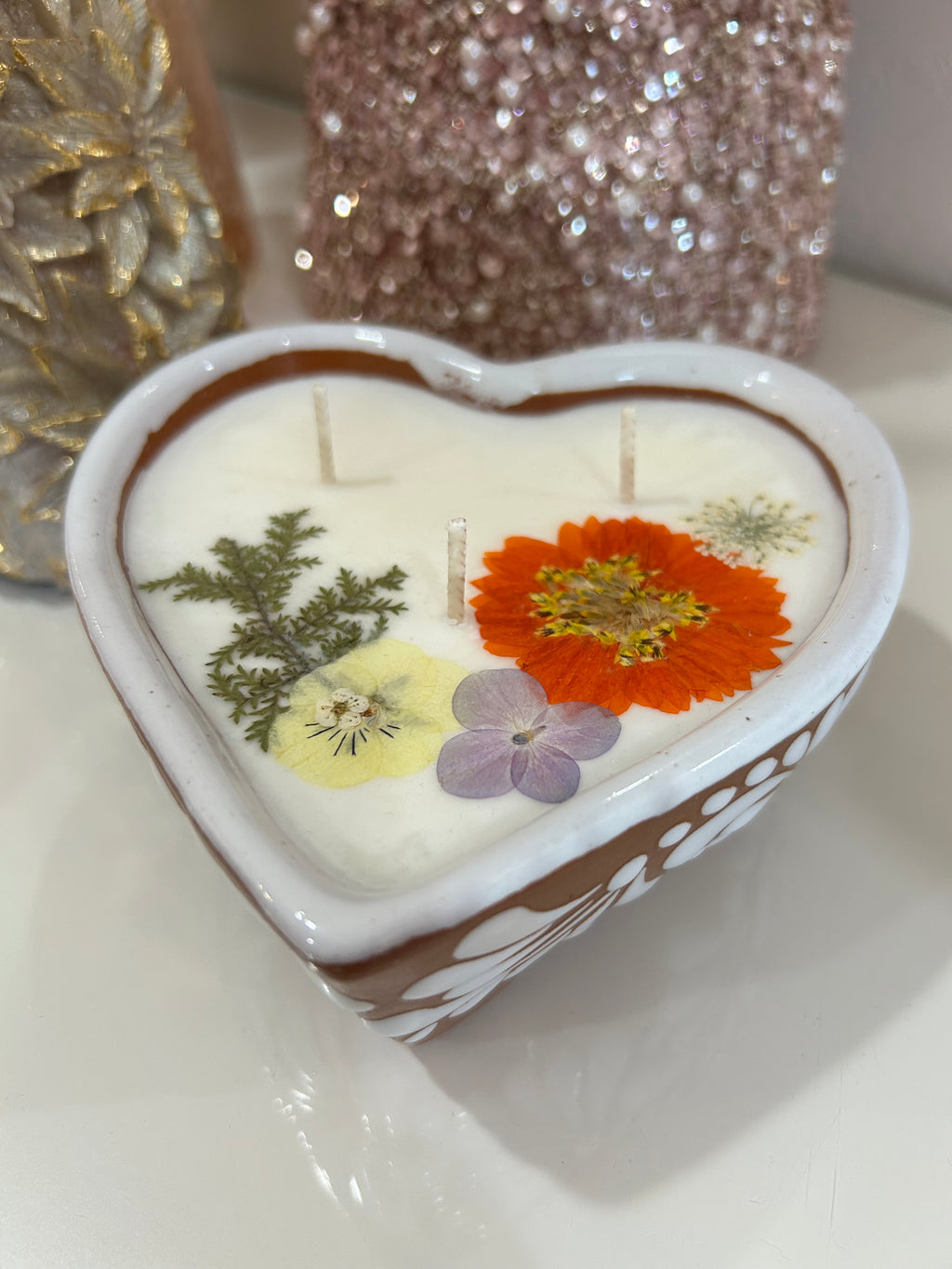 Talavera candle in a heart-shaped container with dried flowers imbedded, on a white background.
