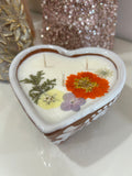 Talavera candle in a heart-shaped container with dried flowers imbedded, on a white background.