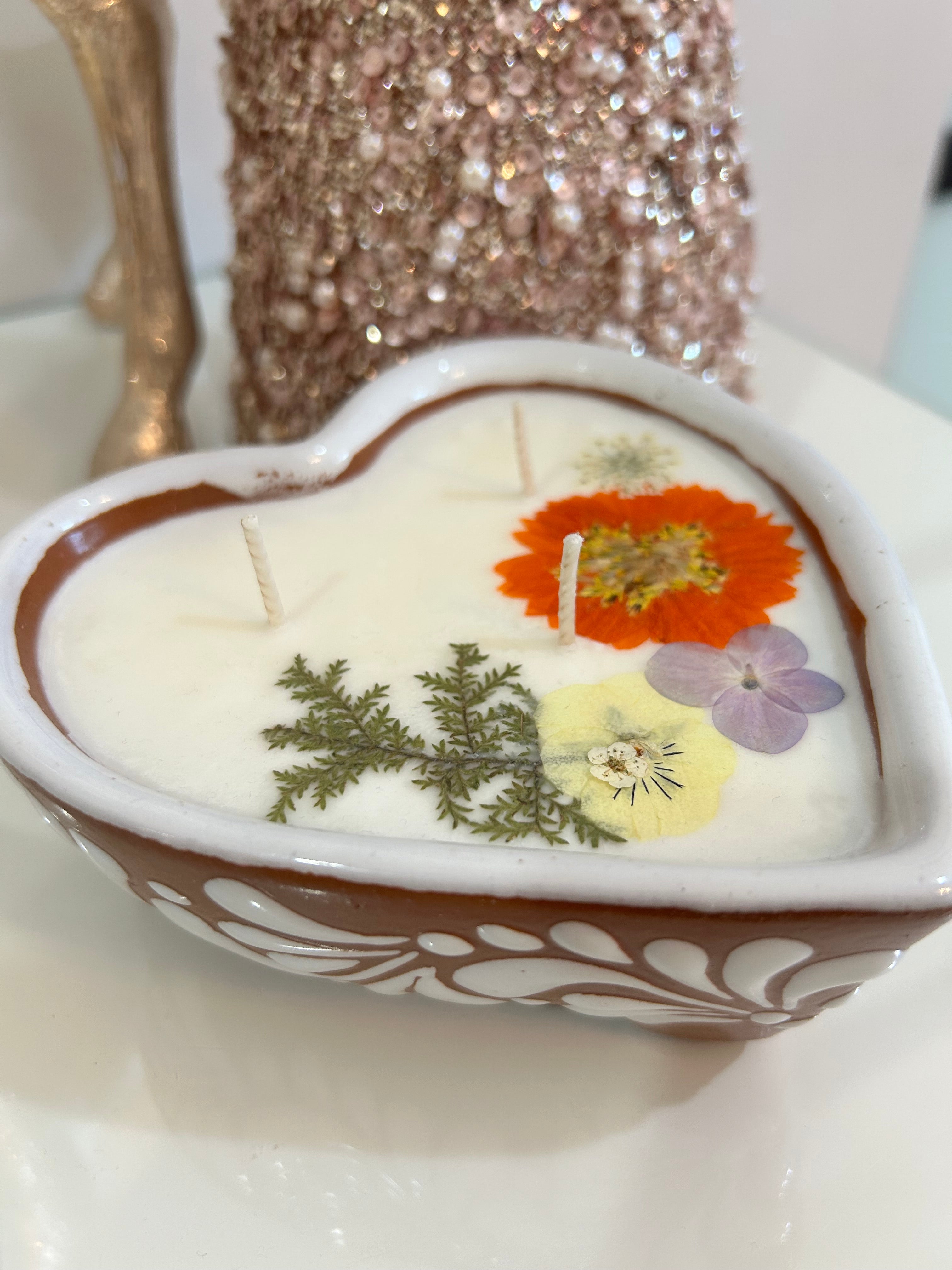 Talavera candle in a heart-shaped container with dried flowers imbedded, on a white background.