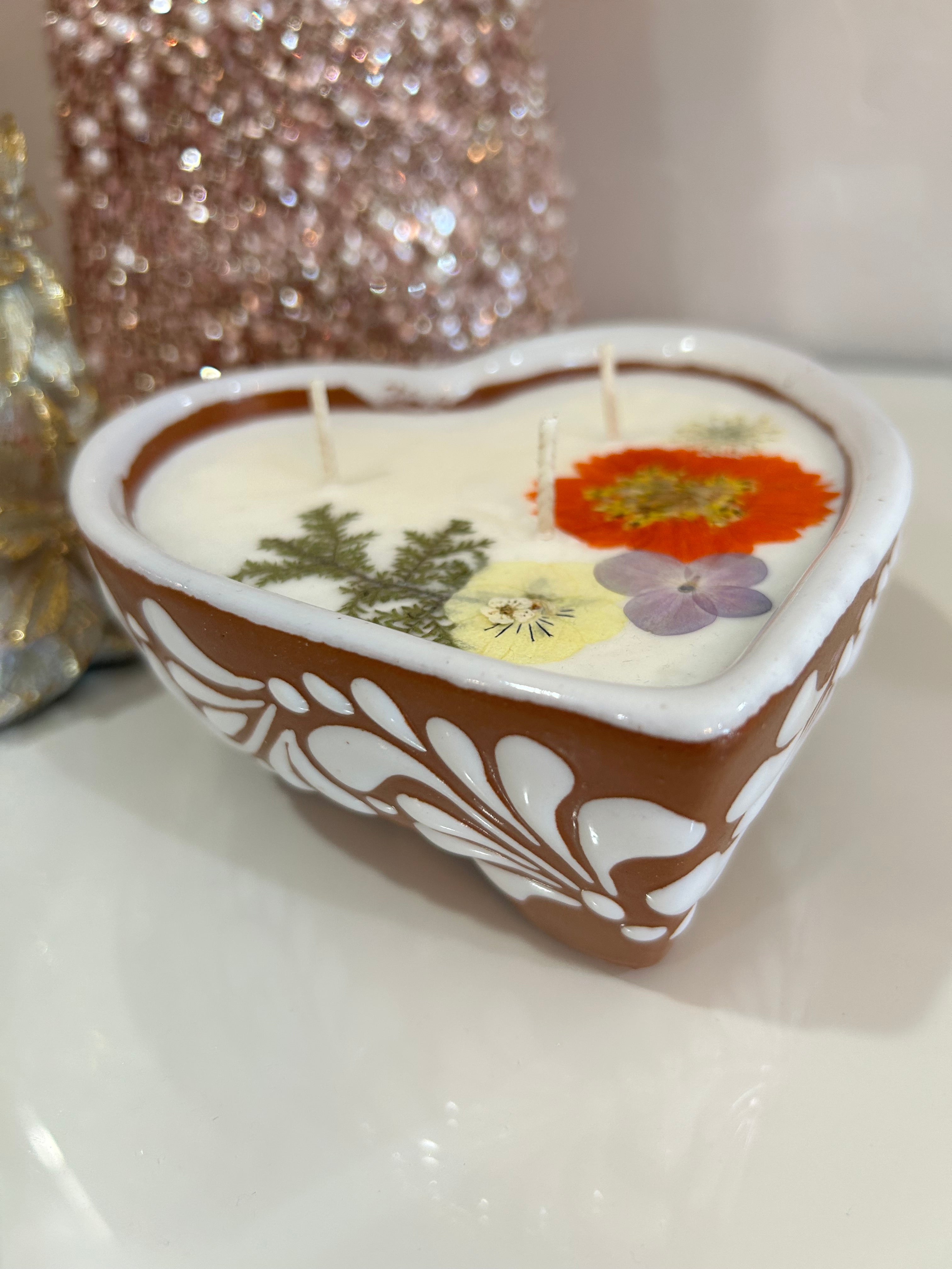 Talavera candle in a heart-shaped container with dried flowers imbedded, on a white background.