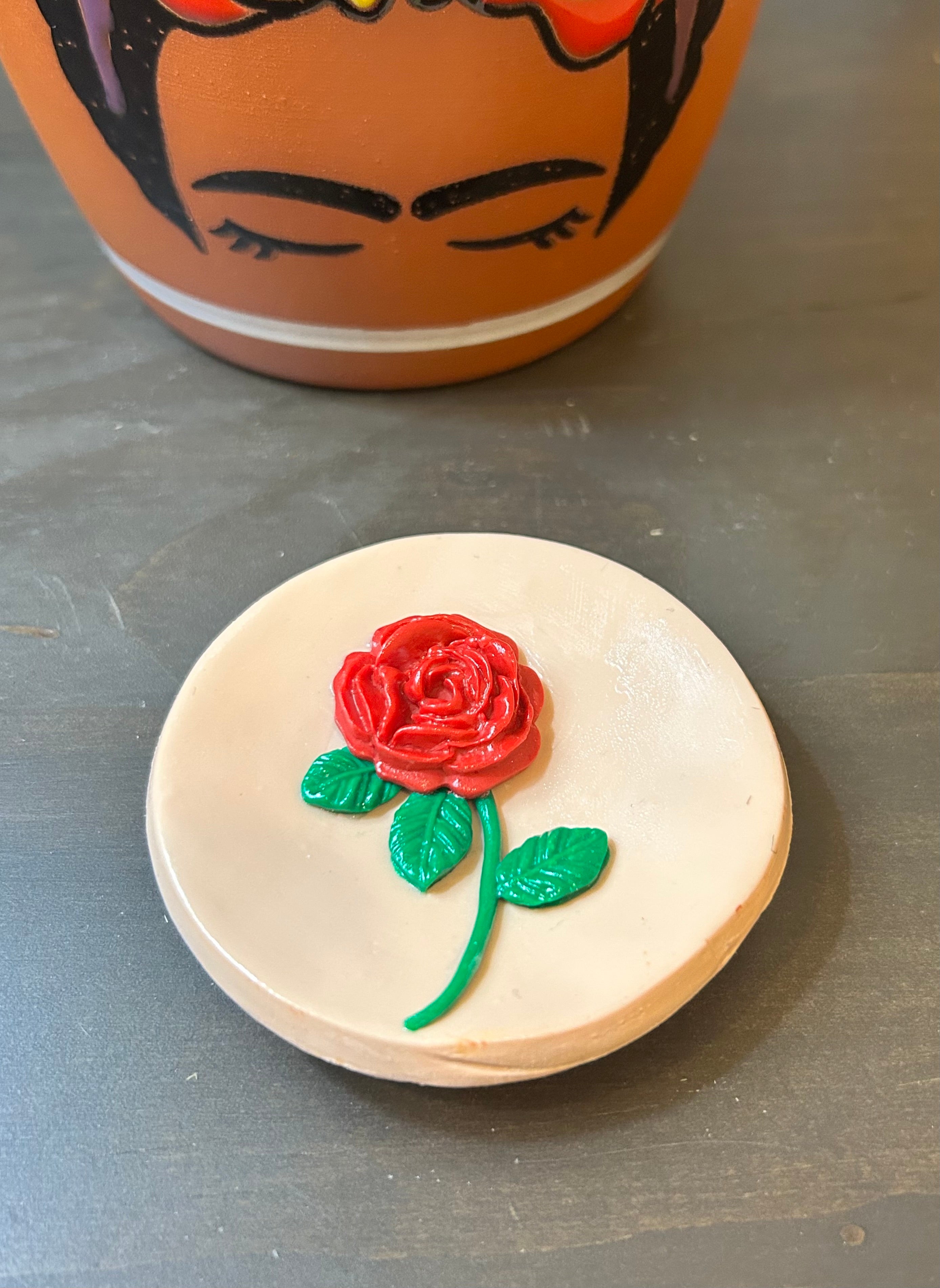 Round Mazapan trinket dish with a centered red rose design on a gray surface.