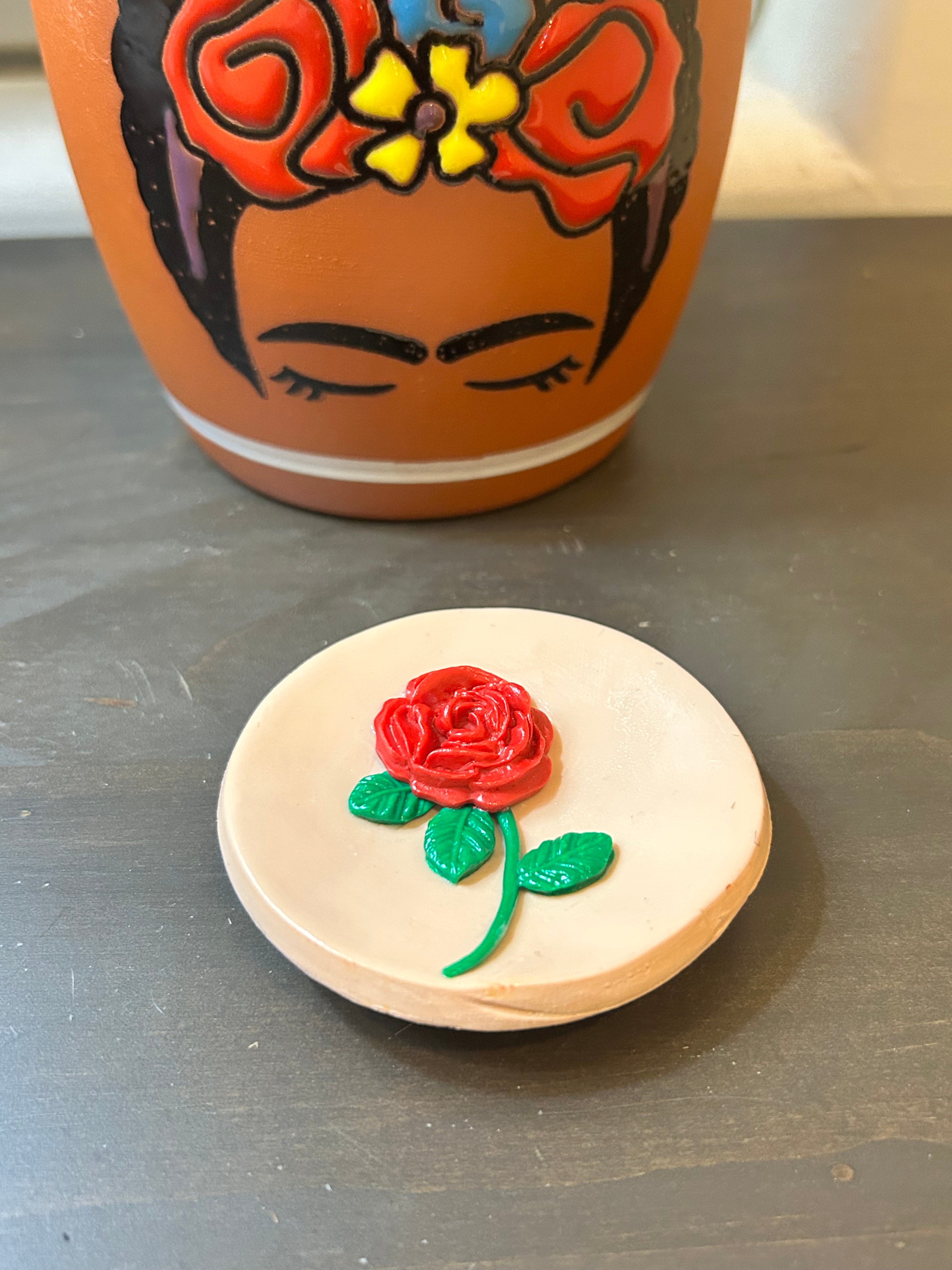 Round Mazapan trinket dish with a centered red rose design on a gray surface.