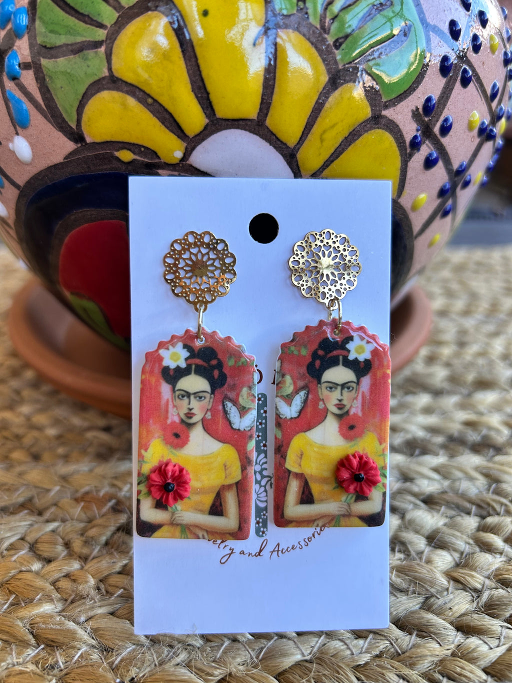 Frida Kahlo-themed earrings on a backing card against a colorful pot.