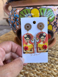 Frida Kahlo-themed earrings on a backing card against a colorful pot.
