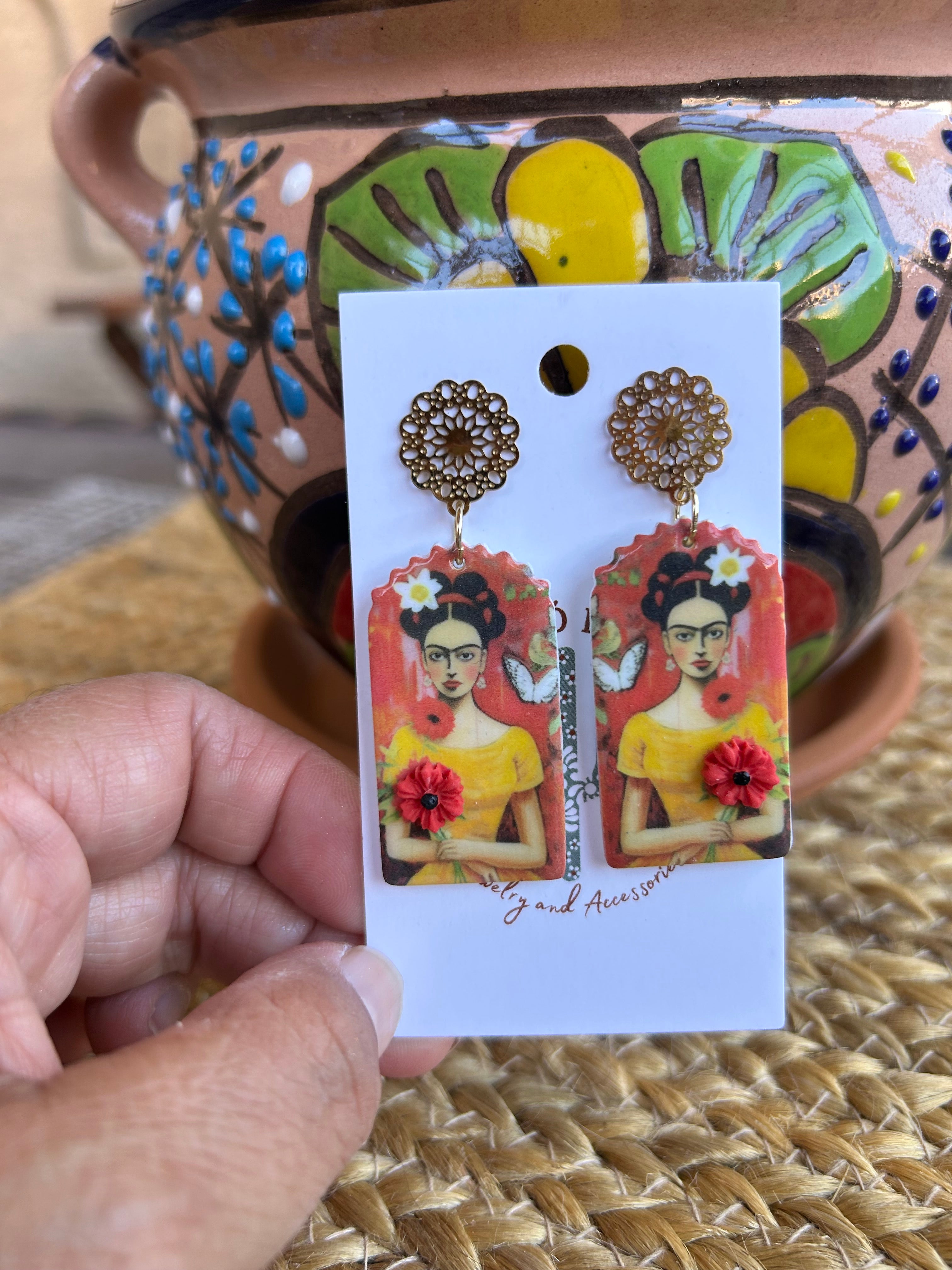 Frida Kahlo-themed earrings on a backing card against a colorful pot.